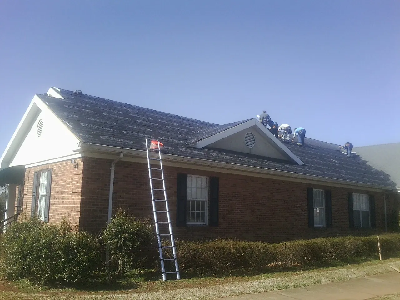 Crew tearing shingles off a brick ranch roof with a ladder set — Metal Roof Repair work by our crew in Lebanon