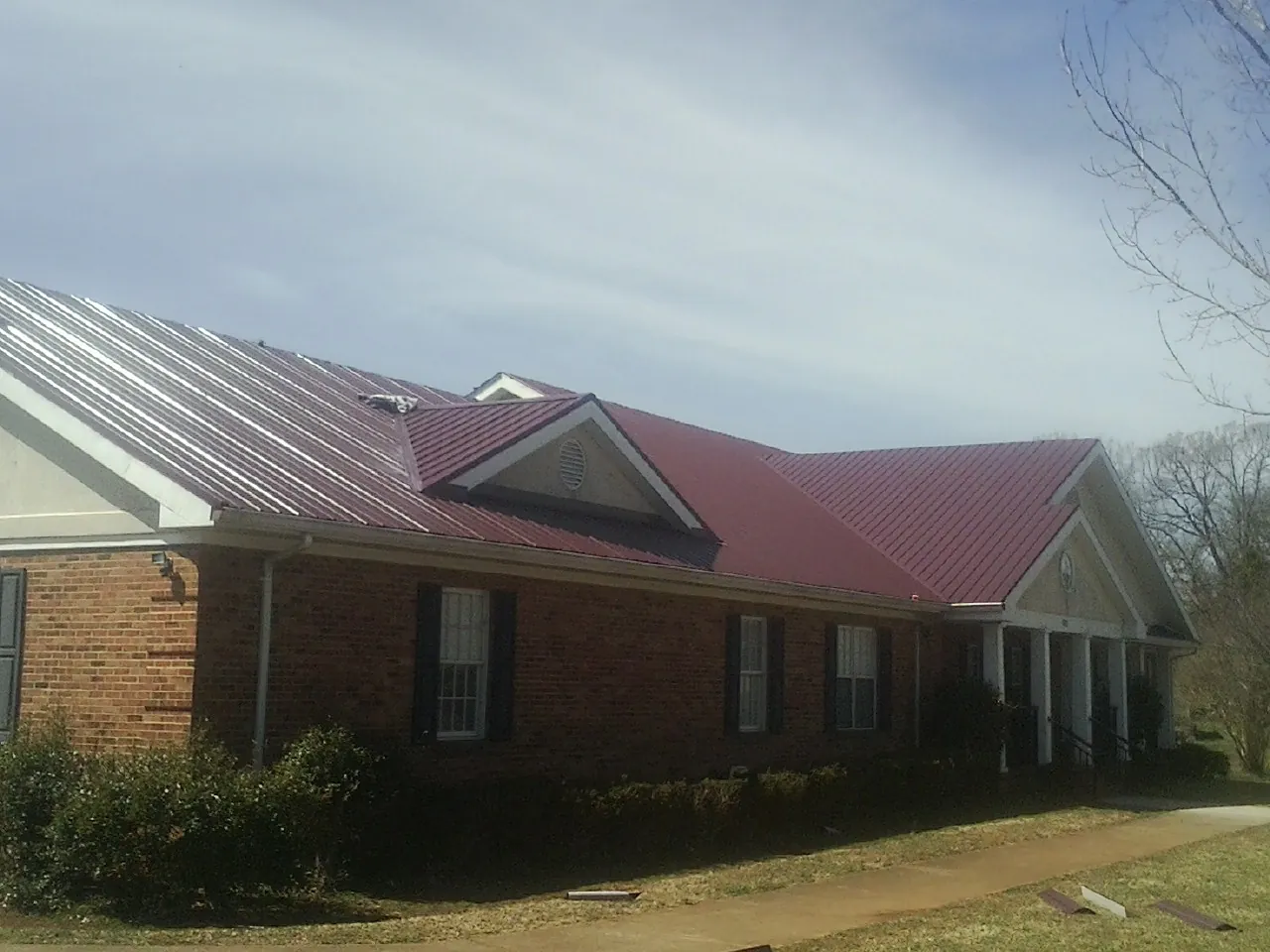 Red metal roof with gabled entries on a long brick building, from a Hail Damage Roof Repair job in Lebanon