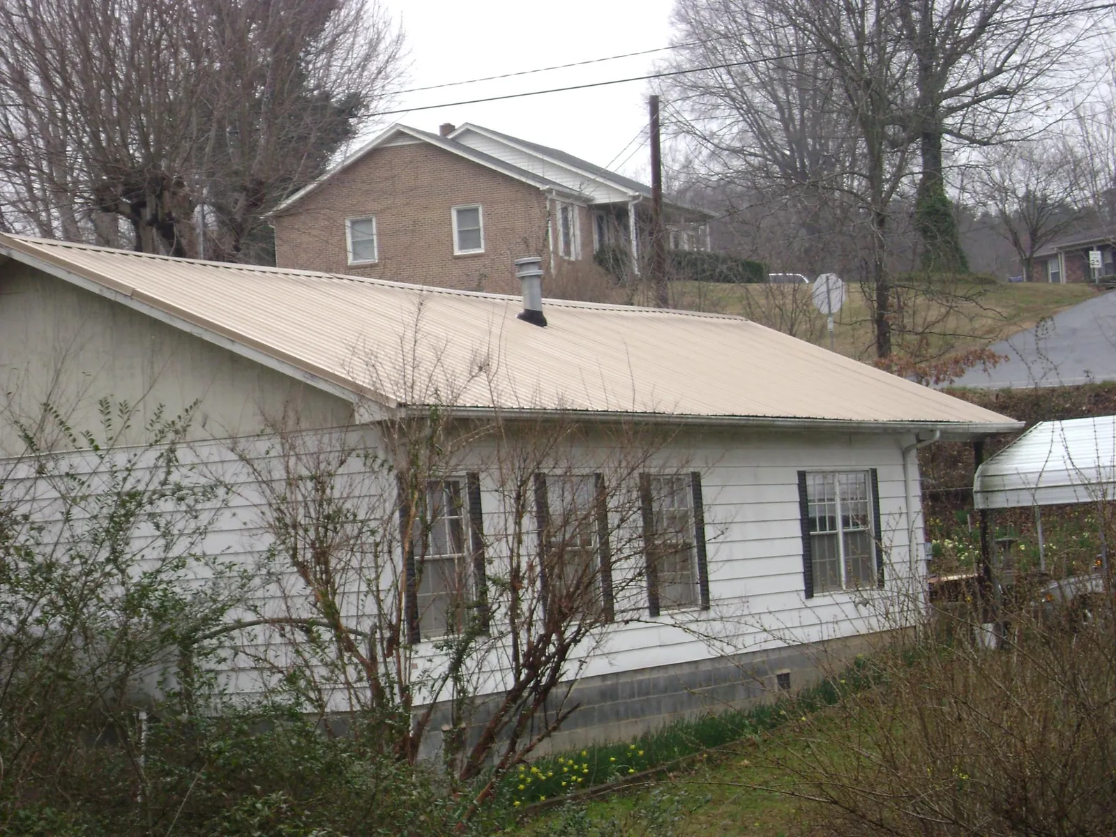 Tan metal roof on a white sided house set into a hillside — Commercial Roofing by Roofing Brothers in Lebanon